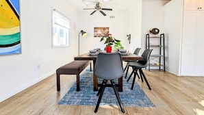 A dining area with a wooden table, chairs, a bench, a potted plant, a painting, and a ceiling fan.
