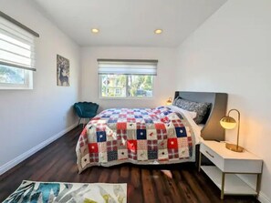 Une chambre à coucher avec un grand lit, une table de chevet, une chaise et une fenêtre avec des stores.