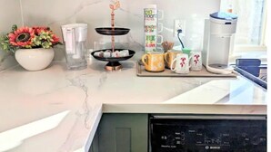 A kitchen counter with a coffee maker, a two-tiered stand with candles, a flower vase, and a coffee machine.