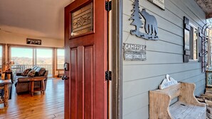A wooden door with a glass panel, a couch, a table, and a bench in a room with wooden floors and a view of mountains through large windows. - Sky's The Limit -Mountain view, golf course, waterfalls, game room. Sleeps 14 (Sky Valley)