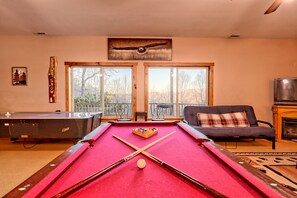 Una mesa de billar en una habitación con ventanales amplios, un sofá y una chimenea.