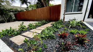 A garden with a gravel path, various plants, and a wooden fence. - Charming, Cozy in the heart of Miami~Near Airport, Brickell, US1 and the Gables  (Miami)