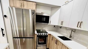 A compact kitchen with a stainless steel refrigerator, a microwave, a stove, and white cabinets. - Charming, Cozy in the heart of Miami~Near Airport, Brickell, US1 and the Gables  (Miami)