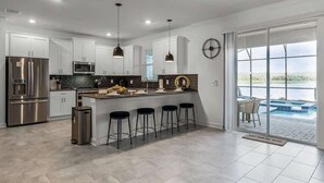 Une cuisine moderne avec des meubles blancs, des appareils en acier inoxydable et un coin bar avec des tabourets.