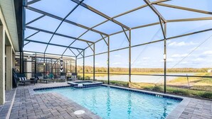 Une piscine extérieure couverte, avec vue sur un lac, entourée d’une terrasse en briques et de chaises longues.