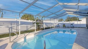 Una piscina interior amb una estructura de sostre blanca, envoltada per una tanca blanca i algunes plantes.