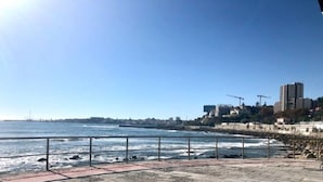 Une promenade en bord de mer, dallée et dotée d’une rambarde, d’où l’on peut admirer un plan d’eau et des bâtiments situés au loin.