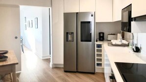 Une cuisine moderne dotée d’appareils électroménagers en acier inoxydable, de meubles blancs et d’une table à manger en bois.
