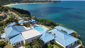 En resort med flere bygninger, blå tage, en swimmingpool og havudsigt.