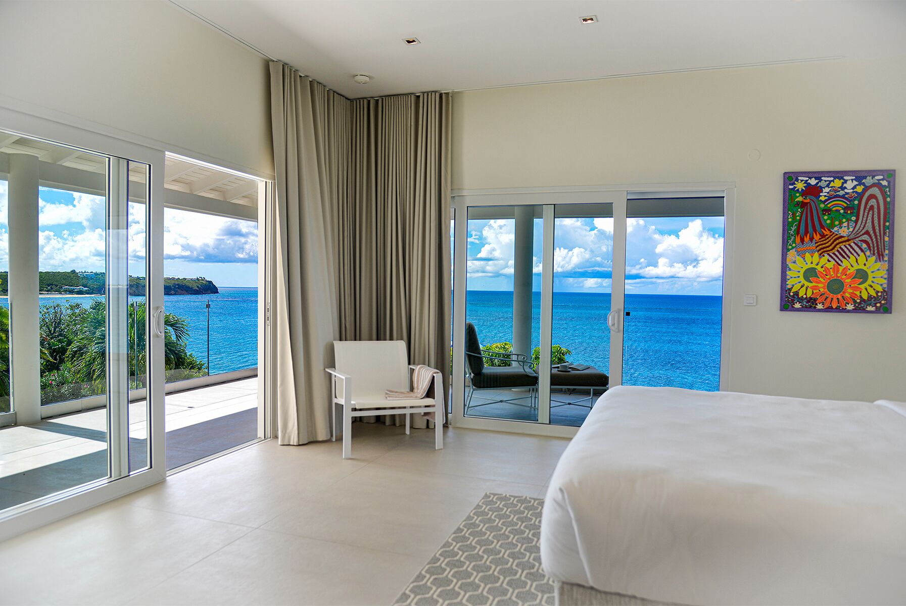 A bedroom with a large bed, a chair, and a view of the ocean through a sliding glass door.