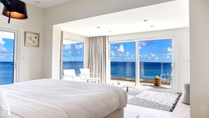 Et moderne hotelværelse med en stor seng, en balkon med havudsigt og et spiseområde med bord og stole.