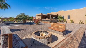 A desert-style outdoor area with a fire pit, wooden benches, and a covered seating area. - Western desert escape, pool, backyard oasis (Phoenix)
