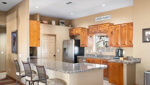 A kitchen with wooden cabinets, granite countertops, a stainless steel refrigerator, and a sign reading "FARMER'S MARKET". - Western desert escape, pool, backyard oasis (Phoenix)