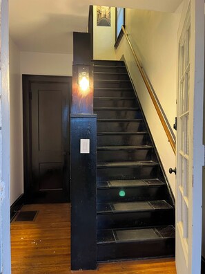 A staircase with a handrail, a light fixture on the wall, and a door at the bottom.