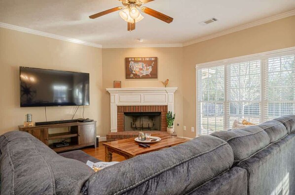 A living room with a large flat-screen TV, a fireplace, and a large window with blinds. - Modern Columbus Military stay w/ Grill & Games (Columbus)