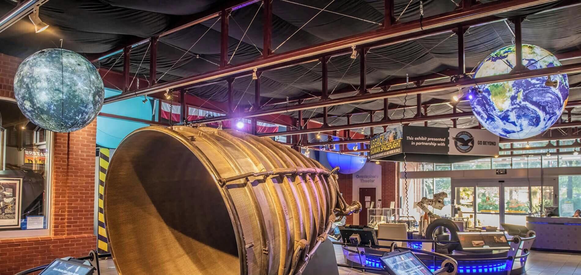 A museum exhibit with a large drum, a hanging globe, and a space shuttle model.