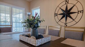 Un comedor con una mesa de madera, individuales tejidos y un centro de mesa con planta en maceta.