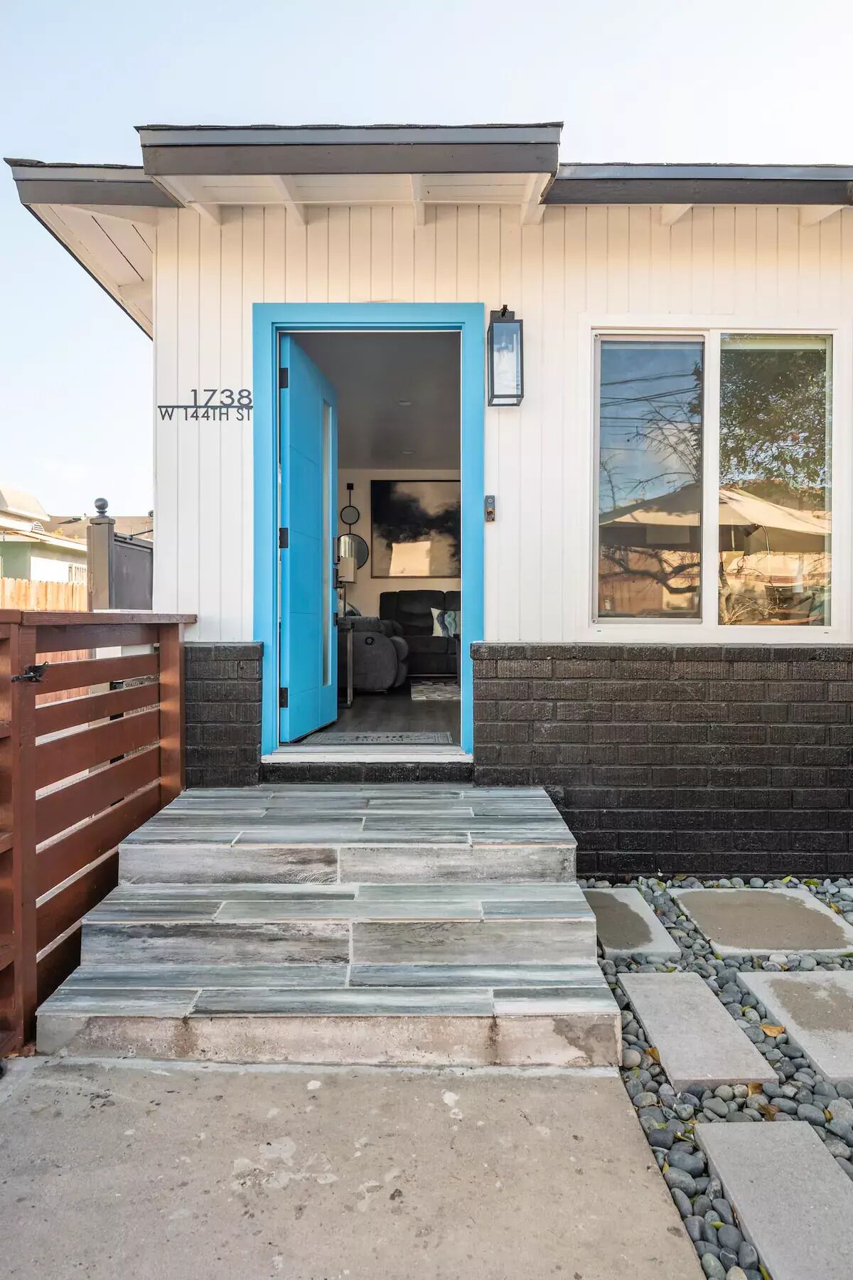 A modern house with a blue door, a stone pathway leading to the entrance, and a brick wall.