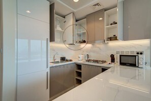 A modern kitchen with white cabinetry, a marble countertop, and built-in appliances including a microwave and coffee maker.