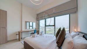 Une chambre moderne avec un grand lit, un bureau et une chaise. Une grande fenêtre offre une vue sur la ville.