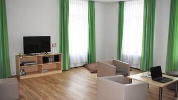 Ein modernes Wohnzimmer mit Flachbildfernseher, einer Holzunterhaltungseinrichtung, einem Laptop auf einem Tisch und grünen Vorhängen.