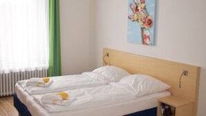 Un dormitorio con cama, mesita de noche, un cuadro y una ventana con cortinas.