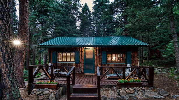 A cabin with a green roof, wooden deck, and stone walls, surrounded by a forest. - Rustic Cozy Cabin at the base of Greenhorn Mountain. (Rye)