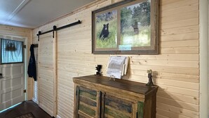 A wooden interior with a sliding door, a framed picture of a bear, and a small cabinet with a paper on top. - Rustic Cozy Cabin at the base of Greenhorn Mountain. (Rye)
