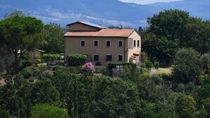 Edifici de dos pisos amb teulada de rajoles vermelles, envoltat de vegetació exuberante i muntanyes al fons.