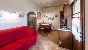 Un espai de vida reduït amb un sofà vermell, una taula de dinar amb cadires, una cuina i una porta de fusta.