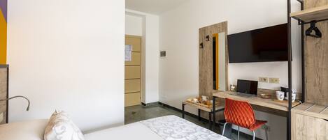 A hotel room with a bed, a desk, a chair, a computer, and a mirror.