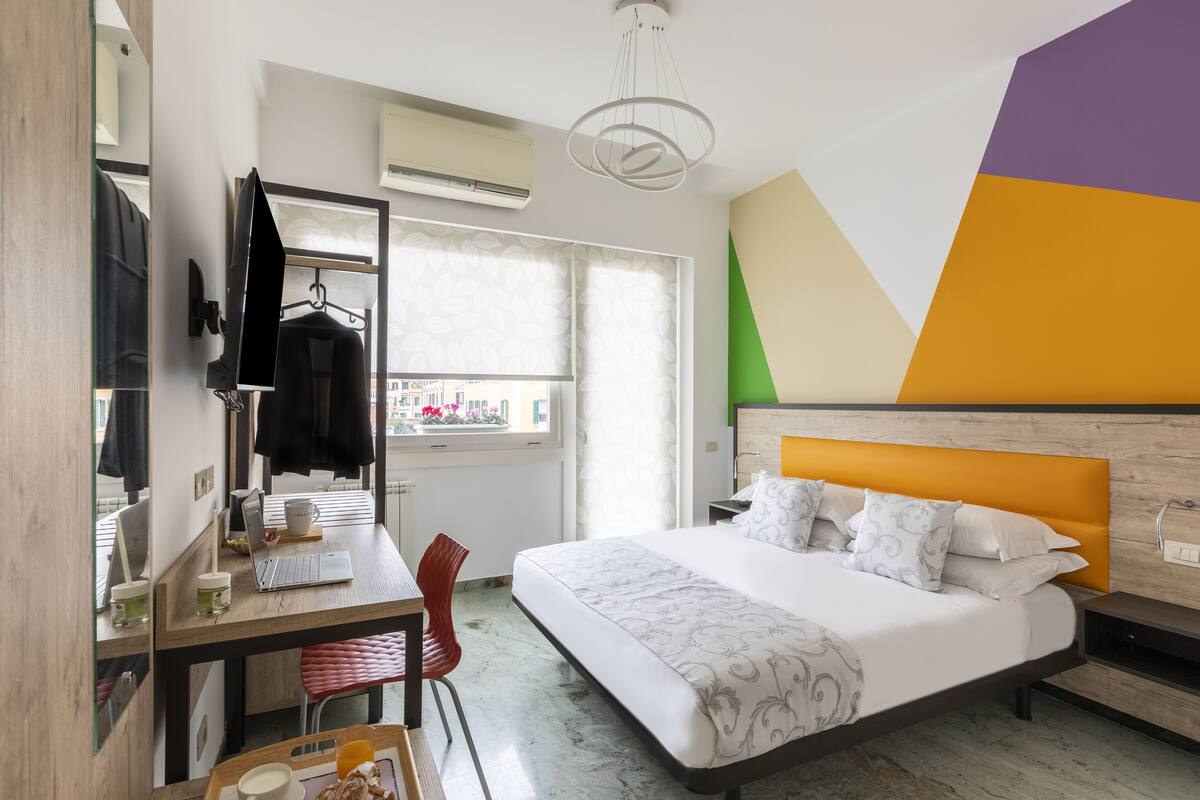 A hotel room with a bed, desk, chair, and a window with curtains.