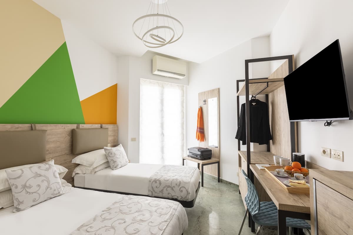 A hotel room with two beds, a desk with a flat-screen TV, a wardrobe, and a window with curtains.