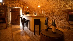Uma adega rústica com paredes de pedra, balcão de madeira e duas garrafas de vinho sobre um barril.