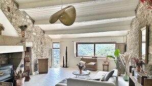 Uma sala de estar ampla com parede de pedra, uma janela grande, um sofá branco e um lustre.