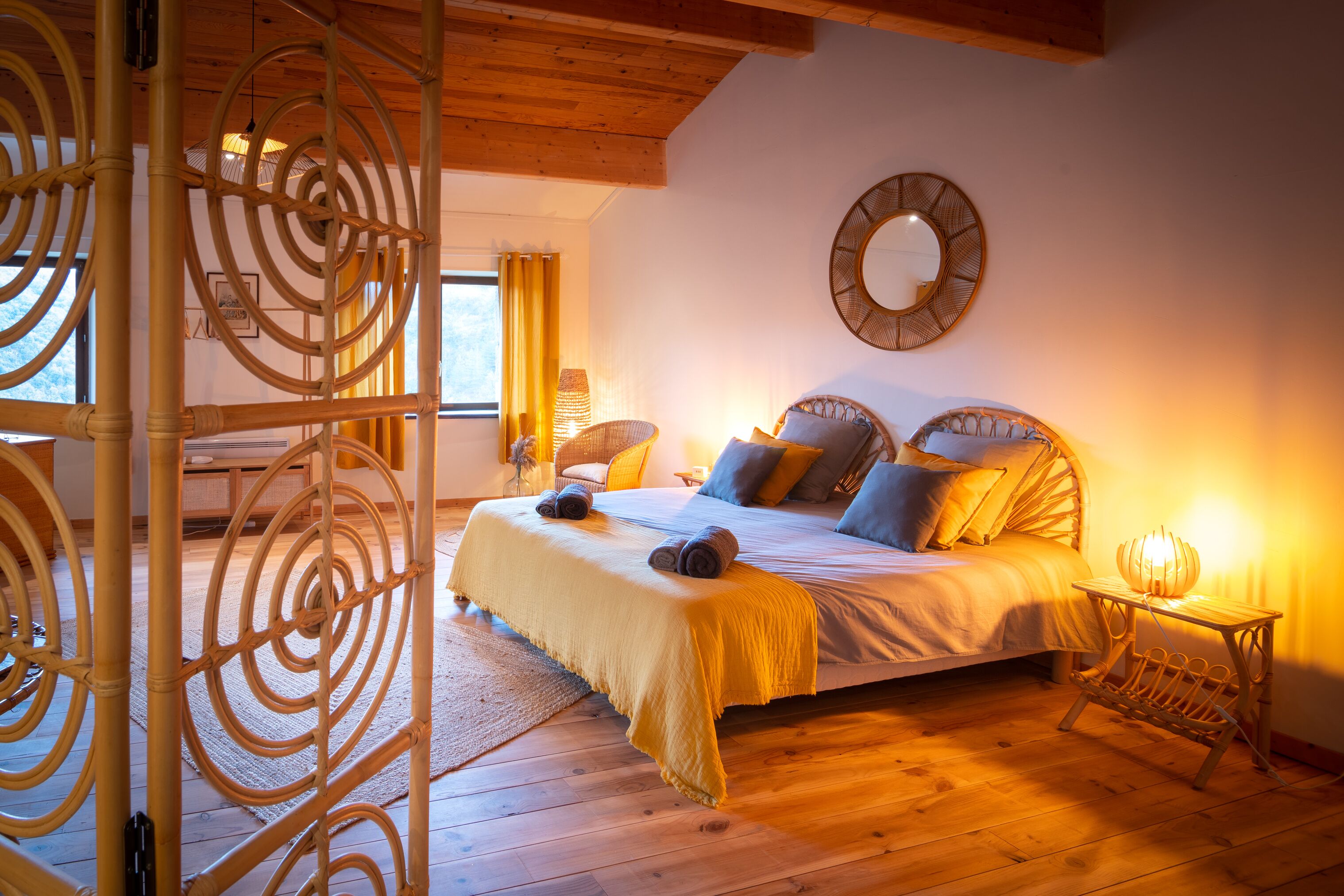 Un dormitorio con cama, una mesita de noche con lámpara, un espejo en la pared y una ventana con cortinas.