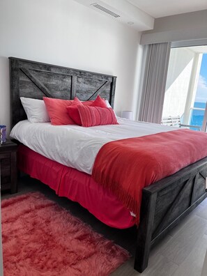 A bedroom with a large bed, a wooden headboard, a red throw blanket, and a fluffy red rug. - Stunning Views - 18th Floor - 1 Bedroom Deluxe (Puerto Peñasco)
