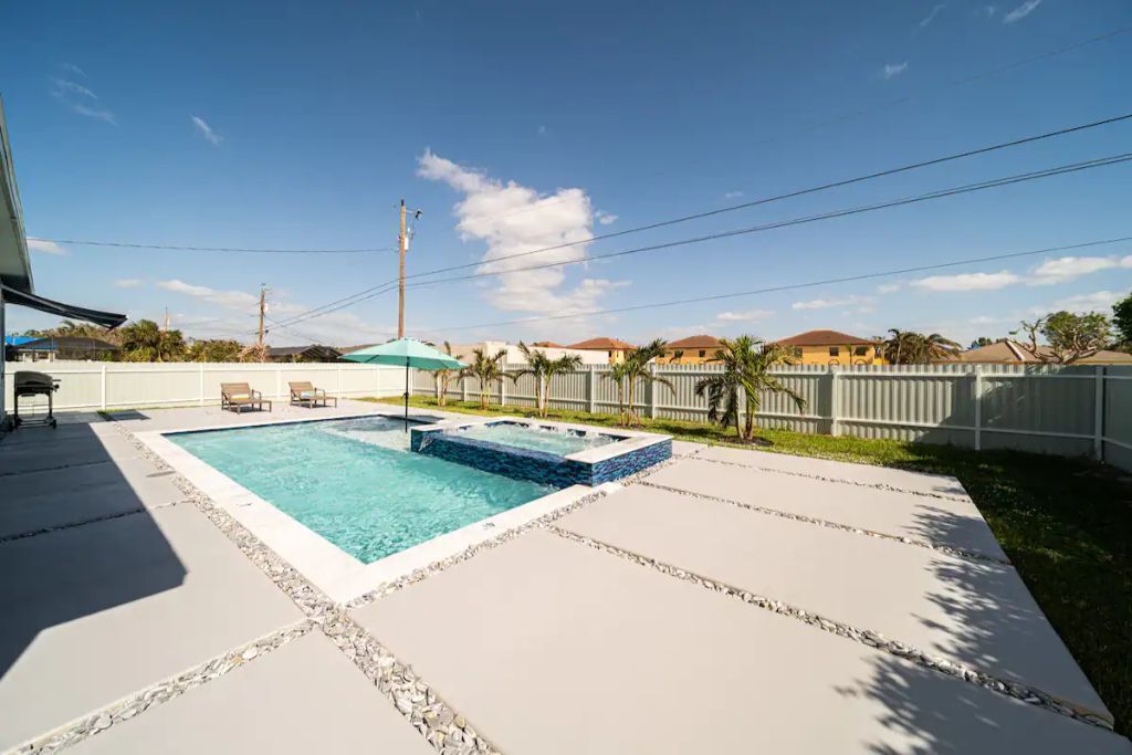 Ein Swimmingpool mit Whirlpool, umgeben von einem weißen Zaun und Palmen.