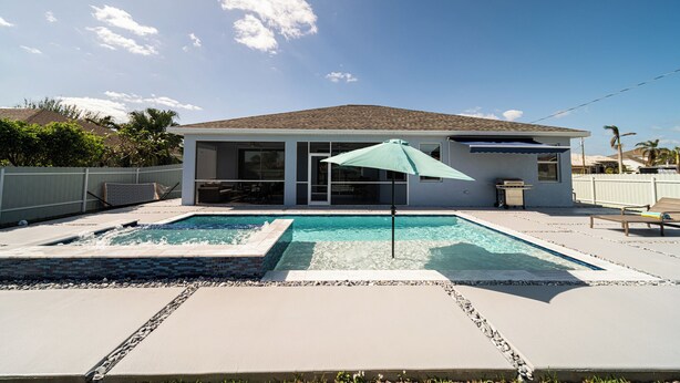 Une maison avec une piscine, un patio et un espace extérieur couvert avec un parasol.