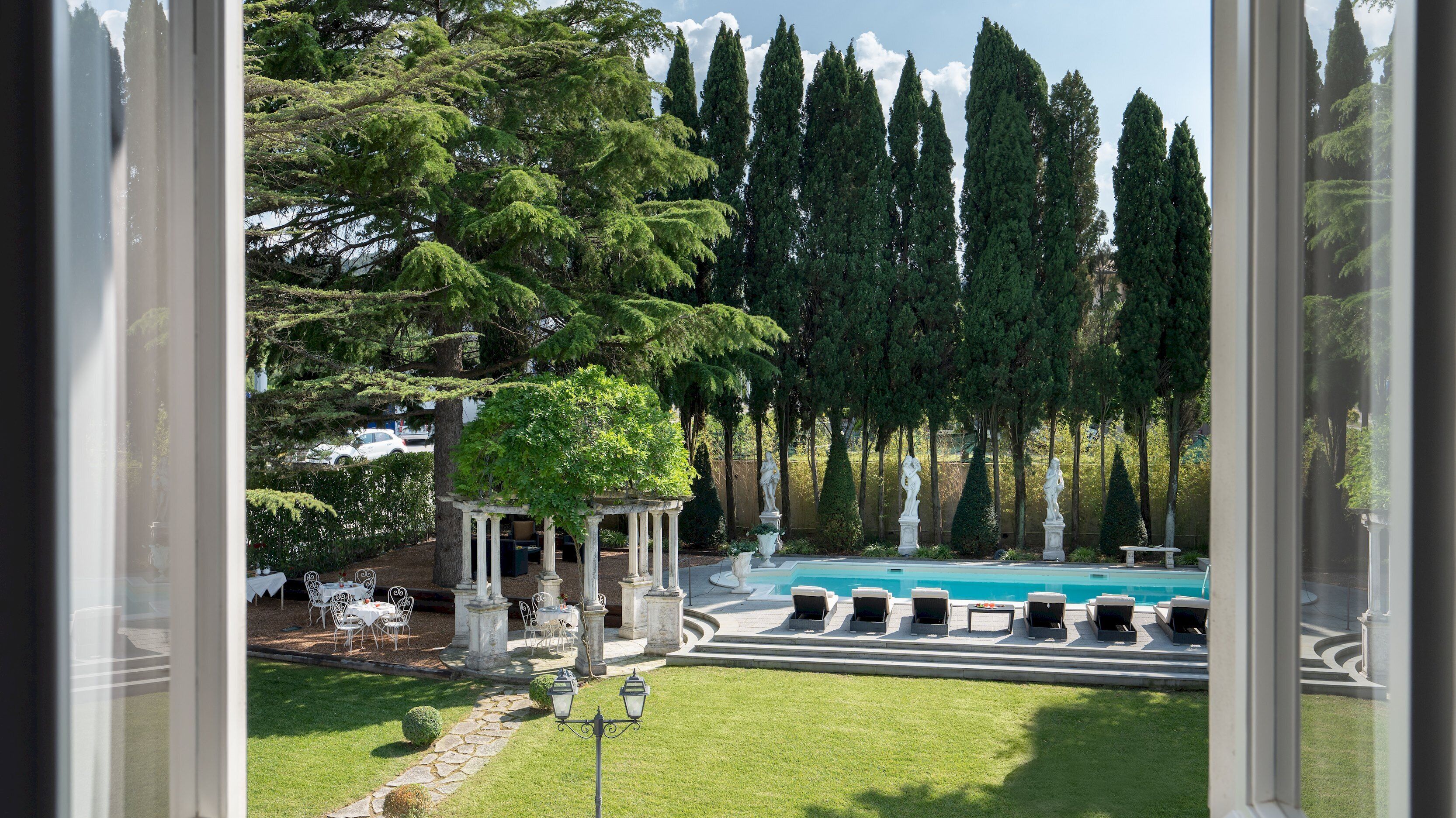Un espace piscine avec des chaises longues, un kiosque et de grands arbres.