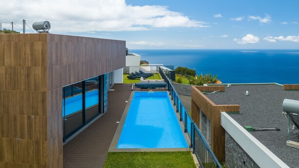 Un edificio moderno con piscina, vista sull'oceano e una zona prendisole con lettini.