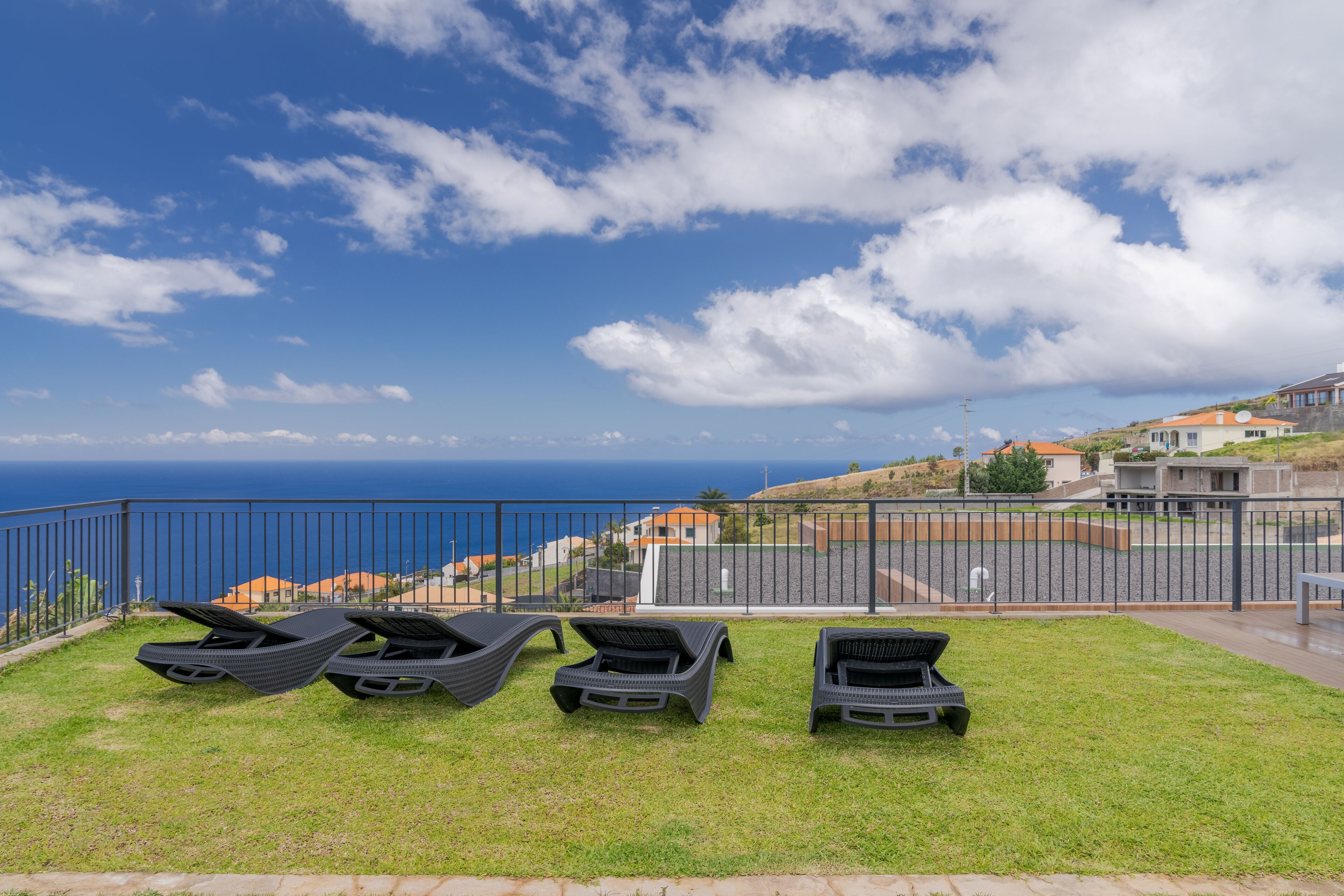 A grassy area with four lounge chairs facing a scenic view of the ocean and hills.