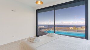 Una camera d'albergo moderna con un'ampia finestra, un letto con asciugamani e vista su una piscina e il paesaggio.
