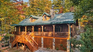 A rustic cabin with a wooden deck, stone foundation, and a chimney. - Family friendly! 3King+Bunk|PingPong|PoolTbl|Private (Pigeon Forge)