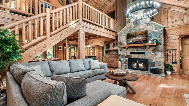 A spacious living area with a large sectional sofa, a wooden staircase, and a stone fireplace. - Family friendly! 3King+Bunk|PingPong|PoolTbl|Private (Pigeon Forge)