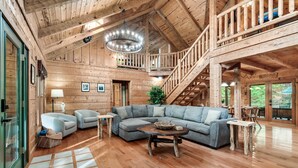 A spacious wooden interior with a large sectional sofa, a chandelier, and a staircase leading to an upper level. - Family friendly! 3King+Bunk|PingPong|PoolTbl|Private (Pigeon Forge)
