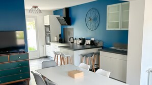 Una cocina moderna con comedor, que presenta una mesa blanca, sillas grises y una pared azul como detalle.