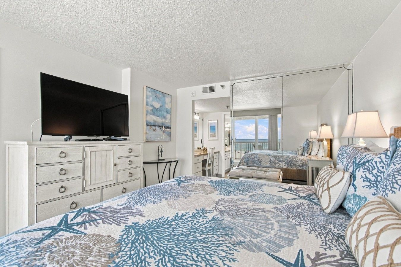 A bedroom with a bed, dresser, television, and a view of the beach.