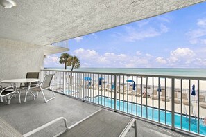 A balcony with a pool, lounge chairs, and a view of the beach and ocean.