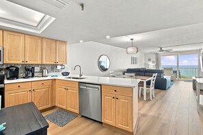 A modern kitchen with wooden cabinets, a dishwasher, and a dining area with a view of the ocean.